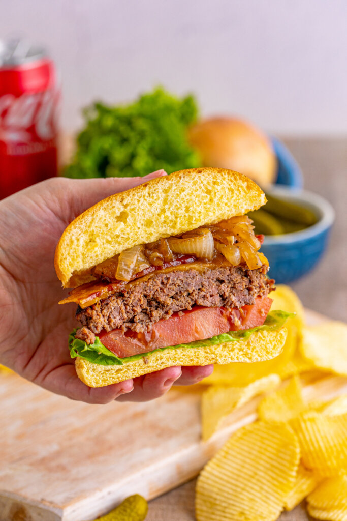 hand holding half of a bacon cheeseburger with ooke onions showing the inside of the sandwich