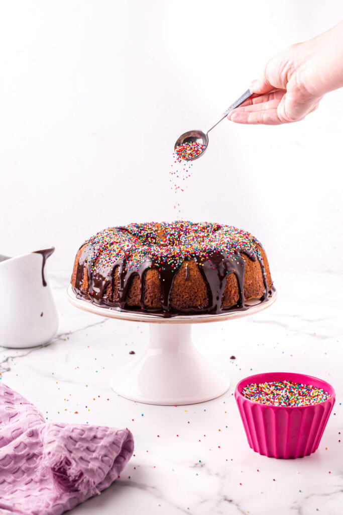 sprinkles being added to the top of a frosted cake