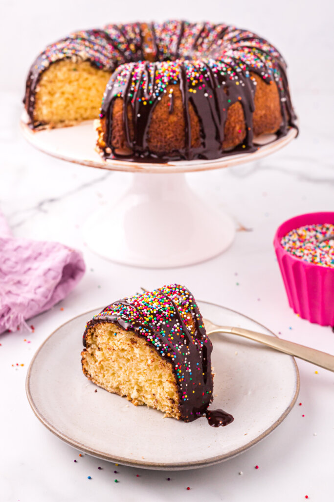 cake slice on plate with melted ice cream bundt cake on cake stand behind