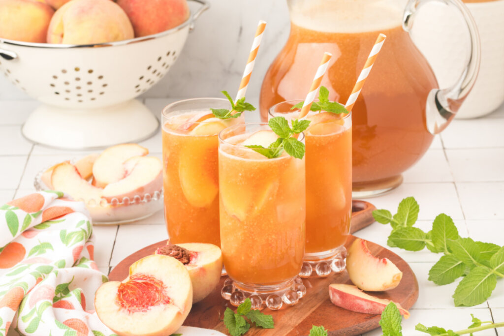 three glasses of peach tea on wooden serving platter with a pitcher of tea in the background