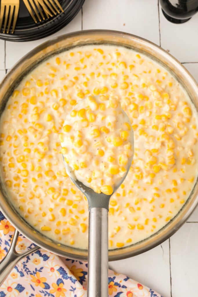 looking down onto a serving spoon with creamed corn over skillet
