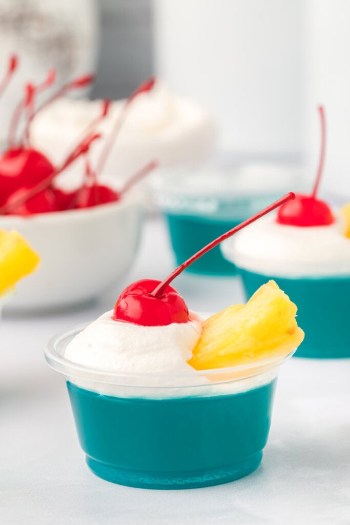 blue hawaiian jello shot topped with whipped cream, pineapple tidbit, and marachino cherry