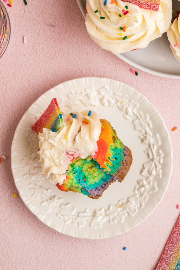 looking down onto a white plate with a frosted rainbow cupcake