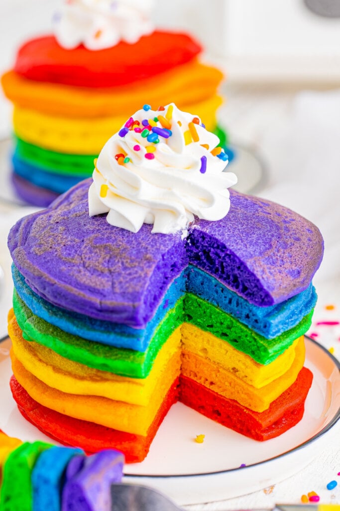stack of rainbow pancakes with a triangle bite taken off the front to show the fluffy inside