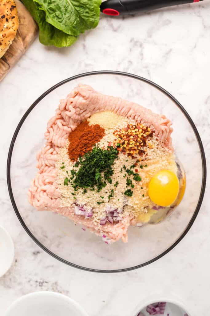 Ground chicken combined with breadcrumbs, egg, red onion, cilantro, and seasonings in a mixing bowl.