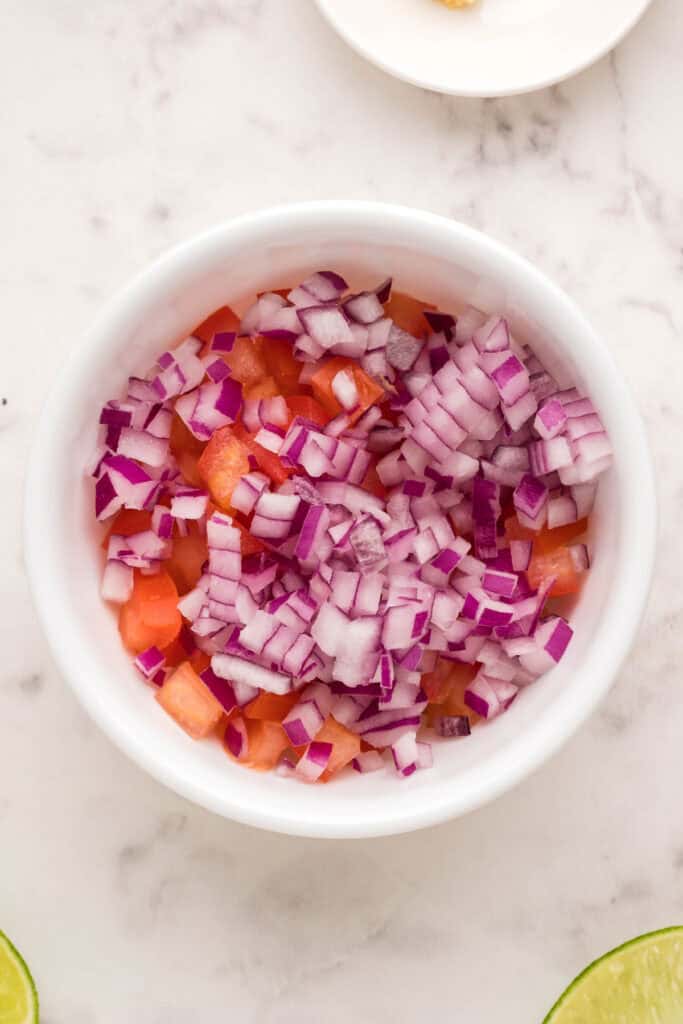 Diced Roma tomato and red onion in a white bowl for fresh salsa topping.