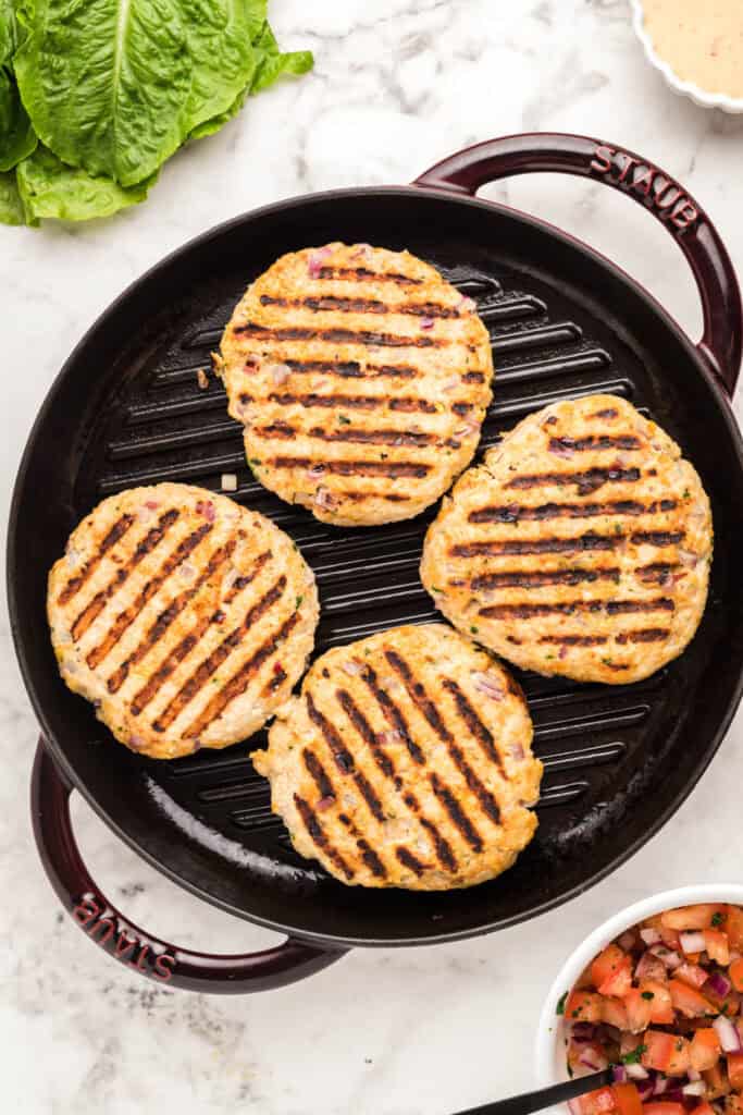 Chicken burger patties cooking on a cast iron grill pan with grill marks.