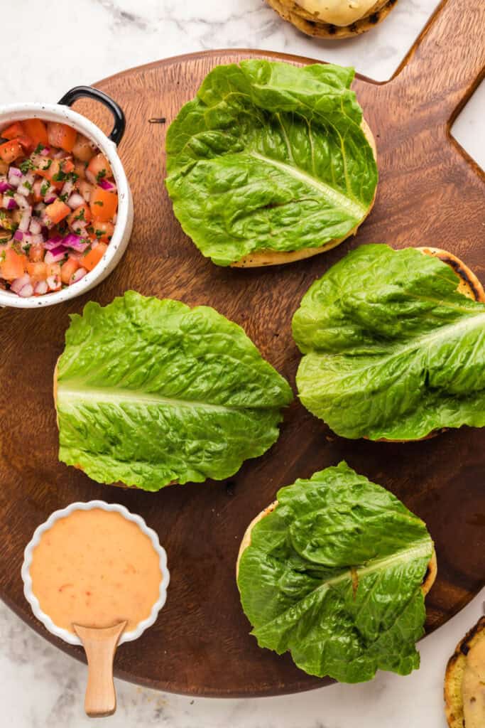 Romaine lettuce leaves added to toasted buns for assembling chicken burgers.