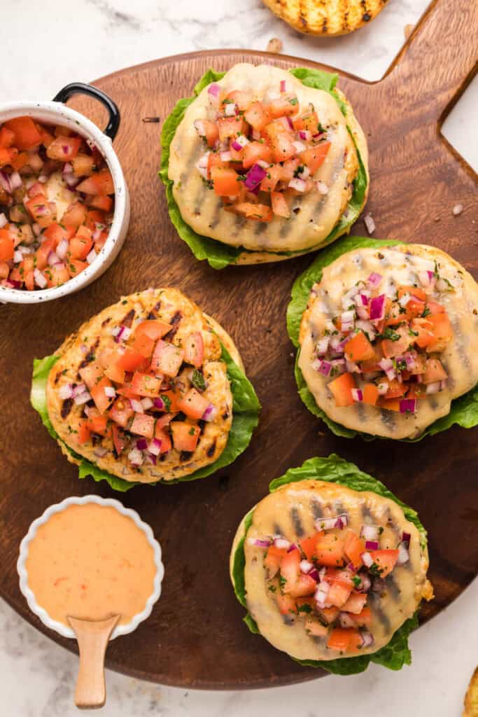 Chicken burgers topped with melted Swiss cheese and fresh tomato salsa on lettuce-lined buns.