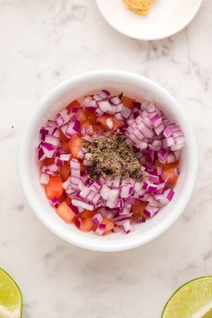 Diced Roma tomato and red onion topped with black pepper in a white bowl.