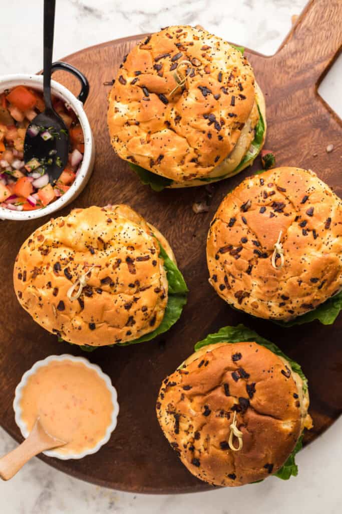 Chicken burgers with bang bang sauce, Swiss cheese, lettuce, and fresh salsa served on toasted onion buns on a wooden board.