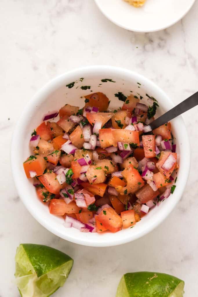 Fresh tomato salsa with red onion, cilantro, lime juice, and black pepper mixed together in a white bowl.