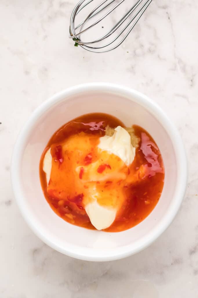 Mayonnaise, sweet chili sauce, hot sauce, and garlic in a white bowl for bang bang sauce.