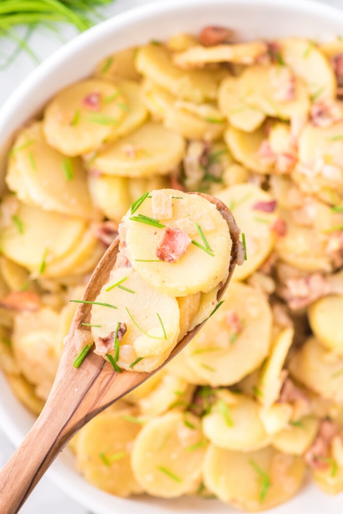german potato salad on wooden spoon over serving bowl