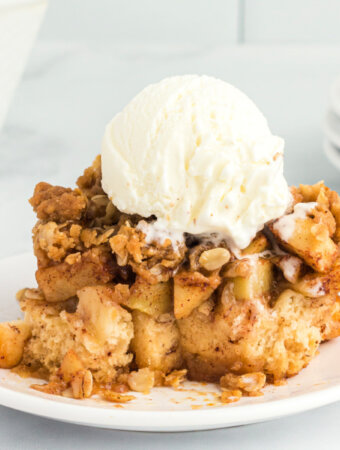 closeup of apple cinnamon roll bake serving on plate topped with a scoop of vanilla ice cream