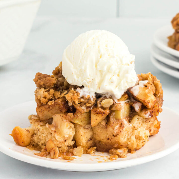 closeup of apple cinnamon roll bake serving on plate topped with a scoop of vanilla ice cream