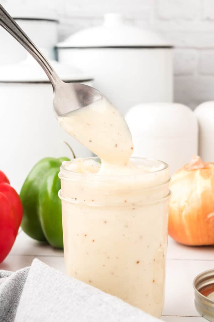 Thick homemade condensed cream soup substitute dripping from a spoon into a glass jar.