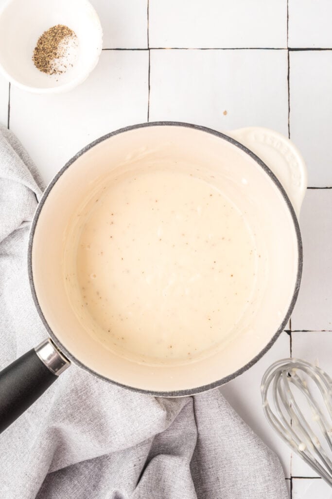 Finished homemade condensed cream soup substitute in a saucepan with a whisk nearby.