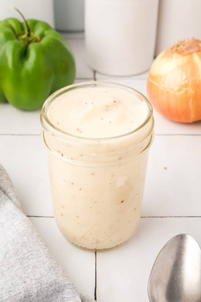 Homemade condensed cream soup substitute stored in a glass jar with bell pepper and onion in the background.