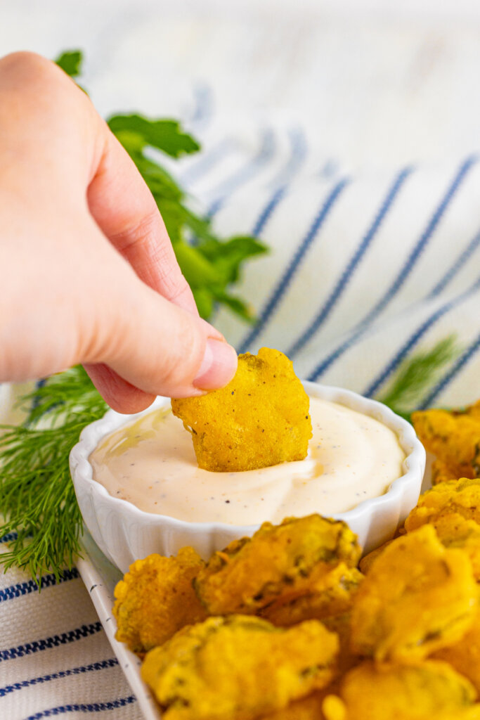 hand dipping a fried pickle into ranch dressing