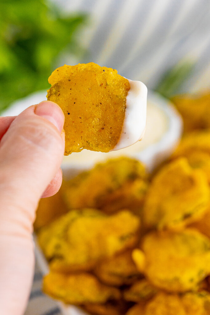 closeup of hand holding a fried pickle with ranch on it