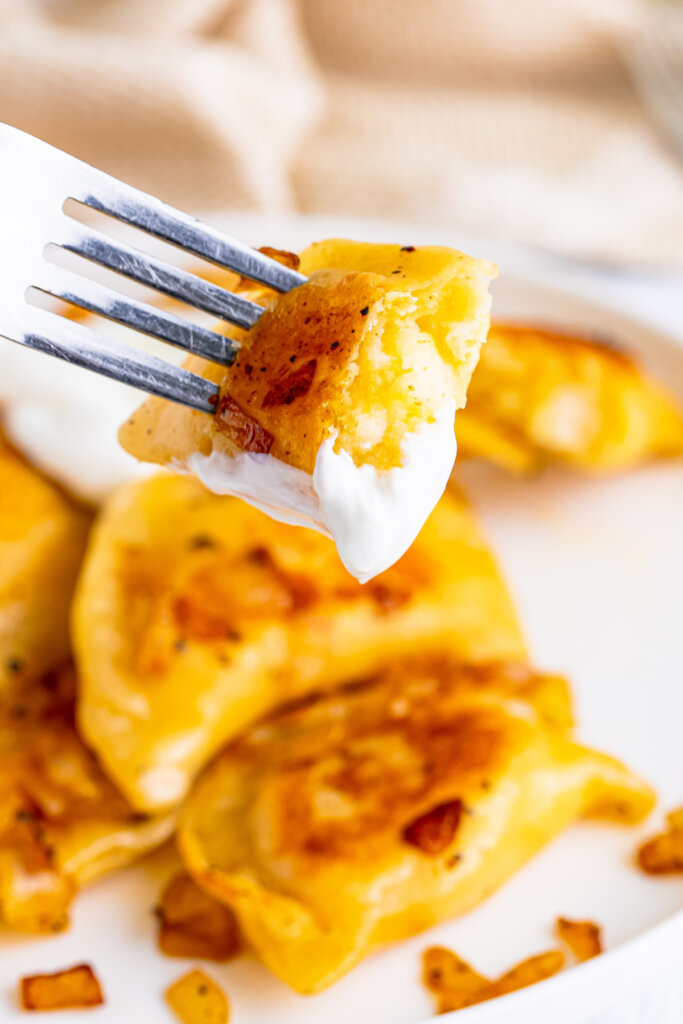 bite of pierogi on a fork with sour cream