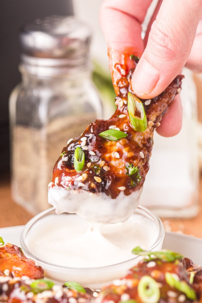 hand holding a teriyaki chicken wing dipped into sauce