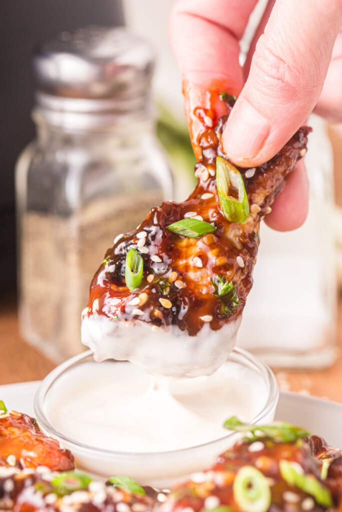 hand holding a teriyaki chicken wing dipped into sauce