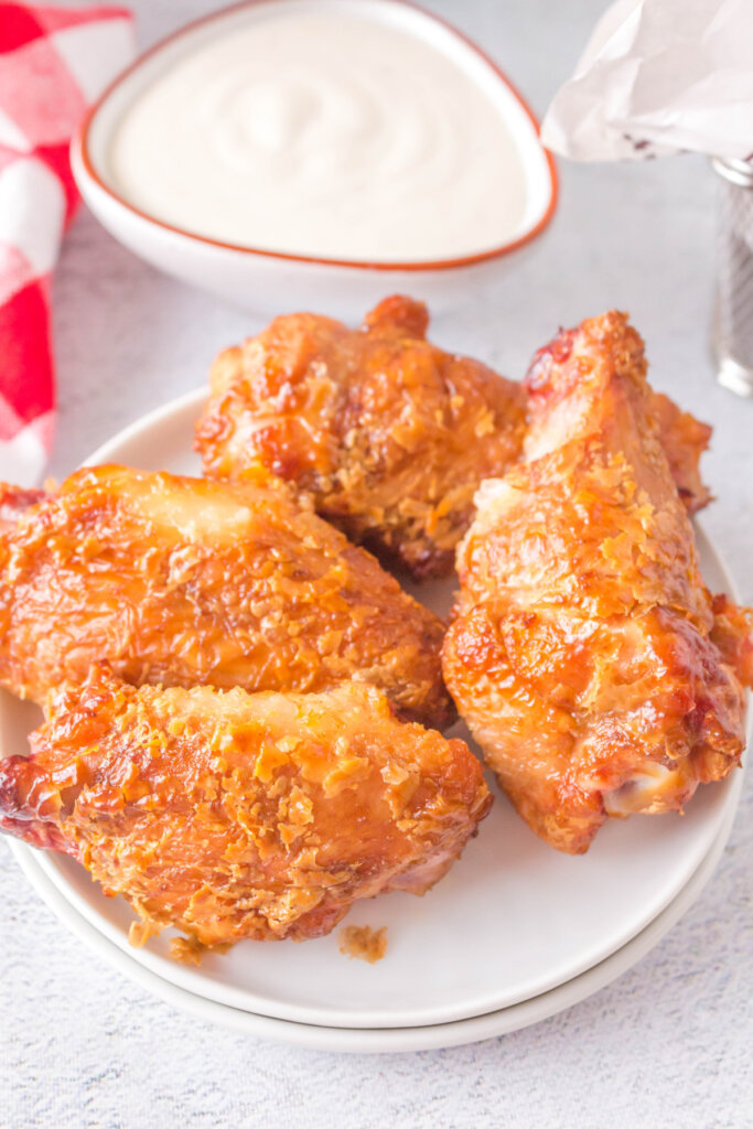 four grilled crispy chicken wings on plate next to dip