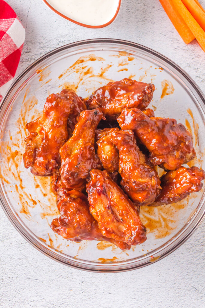 grilled crispy chicken wings in bowl being coated with bbq sauce