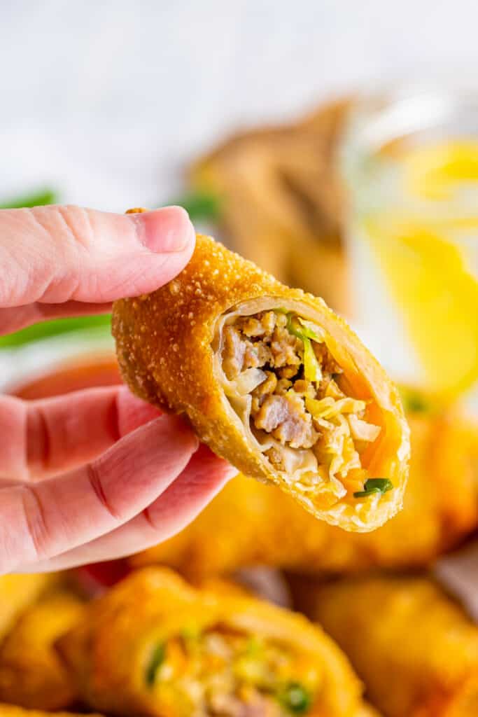 hand holding an egg roll cut in half to show the inside