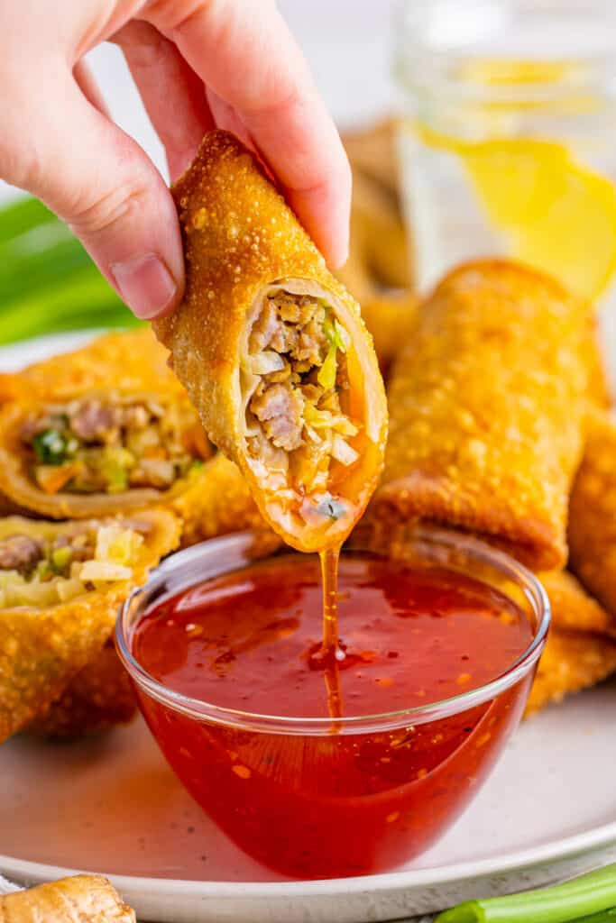 hand dipping an egg roll into chili sauce