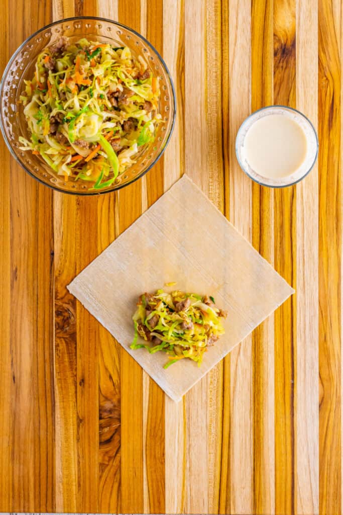 On a clean work surface, place an egg roll wrapper with one of the corners facing you. Add ⅓ cup of the filling to the bottom corner of the wrapper.