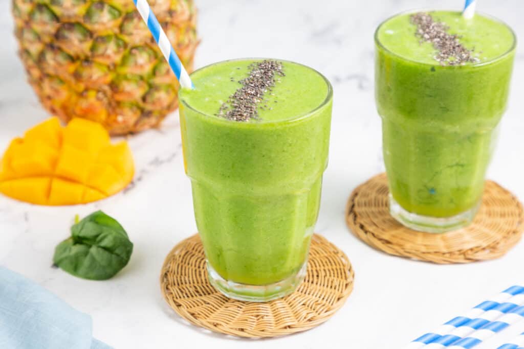 two pineapple green smoothies with fresh fruit on the side