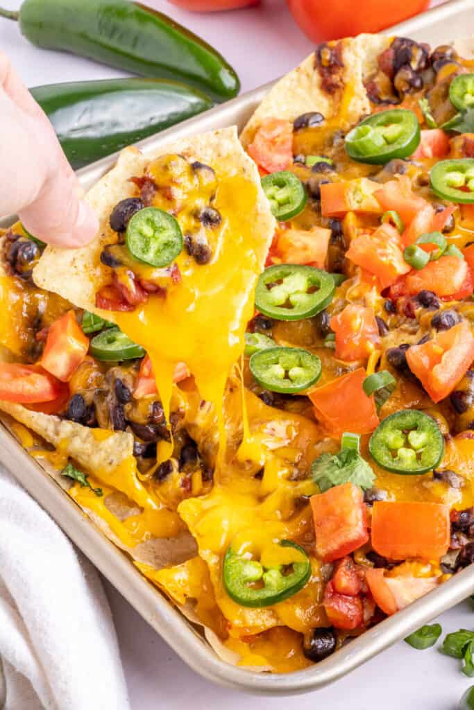 hand pulling a spicy loaded black bean nacho from the sheet pan