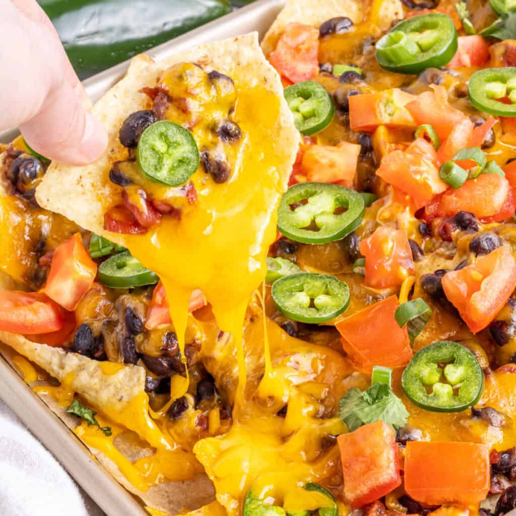 hand lifiting loaded nacho from sheet pan