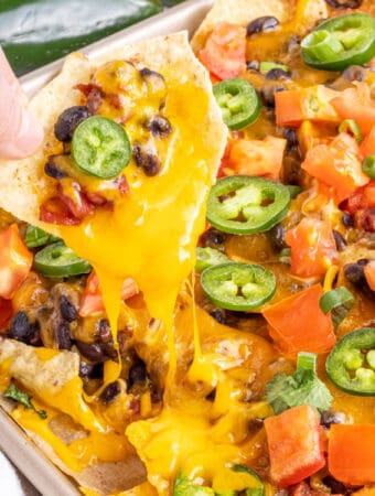 hand lifiting loaded nacho from sheet pan