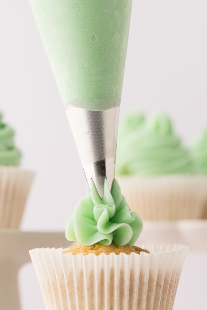 swiss meringue buttercream being piped onto a vanilla cupcake
