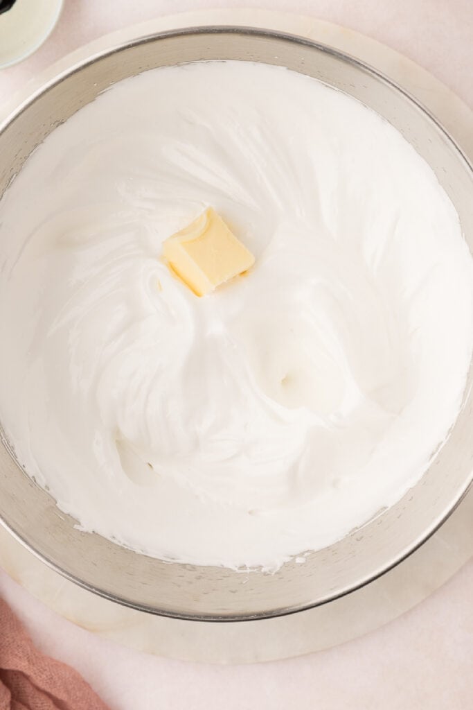 When the outside of the bowl is cool, add the butter a tablespoon at a time. Beat at high speed, fully incorporating each addition of butter until all the butter has been added.