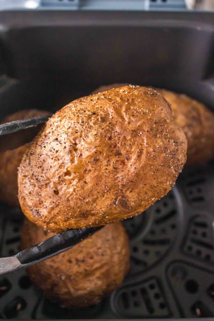 tongs holding an air fryer baked potato over the air fryer basket