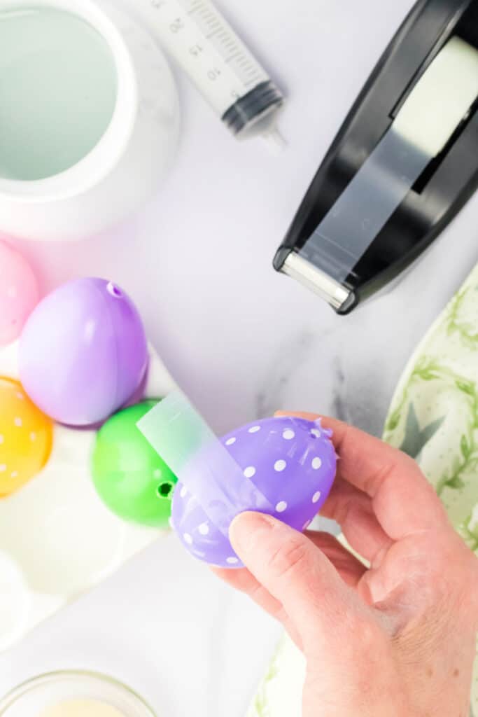 Put the two sides of the egg together and seal the seams using scotch tape.  A lot of the plastic Easter eggs have drainage holes, be sure to cover those with tape too.  Set in the holder and aside for now.  Leave open the hole that you made (or made larger).