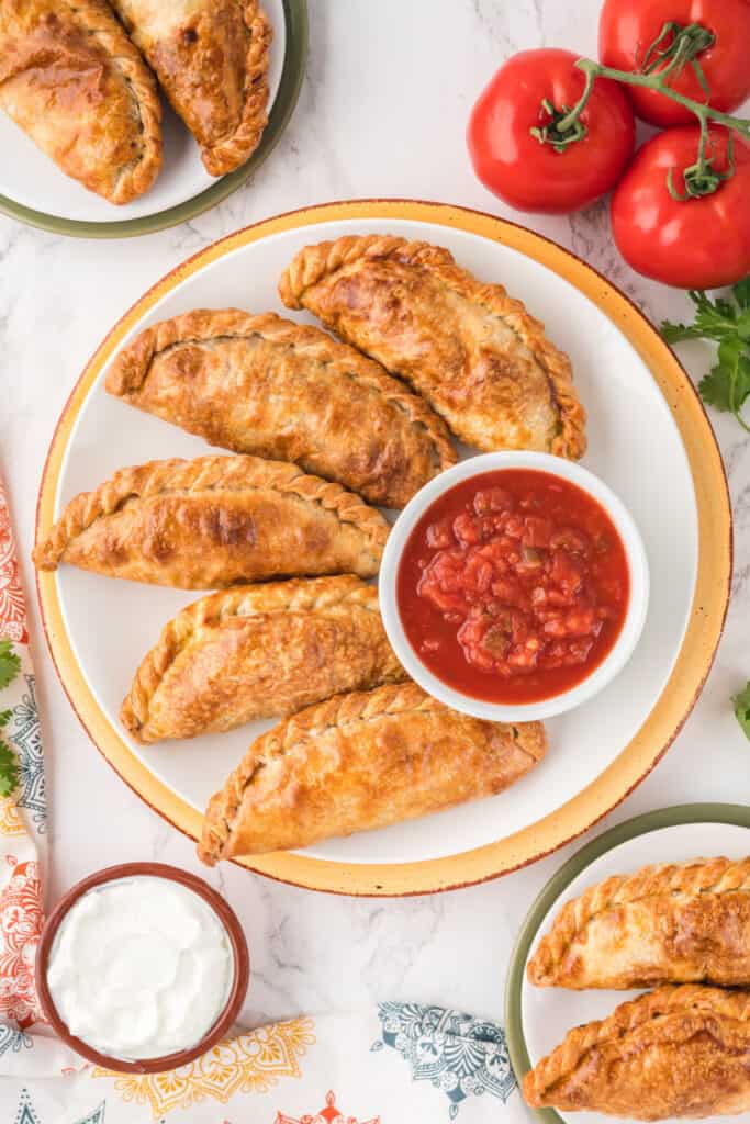 five beef empanadas on a plate with a bowl of salsa