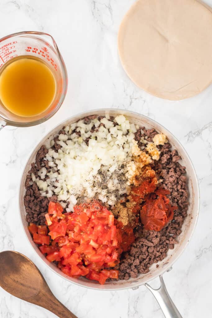 Add diced onion, minced garlic, tomato paste, tomatoes, cumin, chili powder, paprika salt, and pepper to the skillet with the ground beef. Cook for an additional 2-3 minutes until the onion is softened.