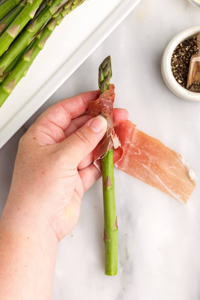 Wash and dry asparagus. Break or cut woody ends off asparagus. Cut prosciutto in half, lengthwise. Wrap prosciutto in a spiral around asparagus stalk.