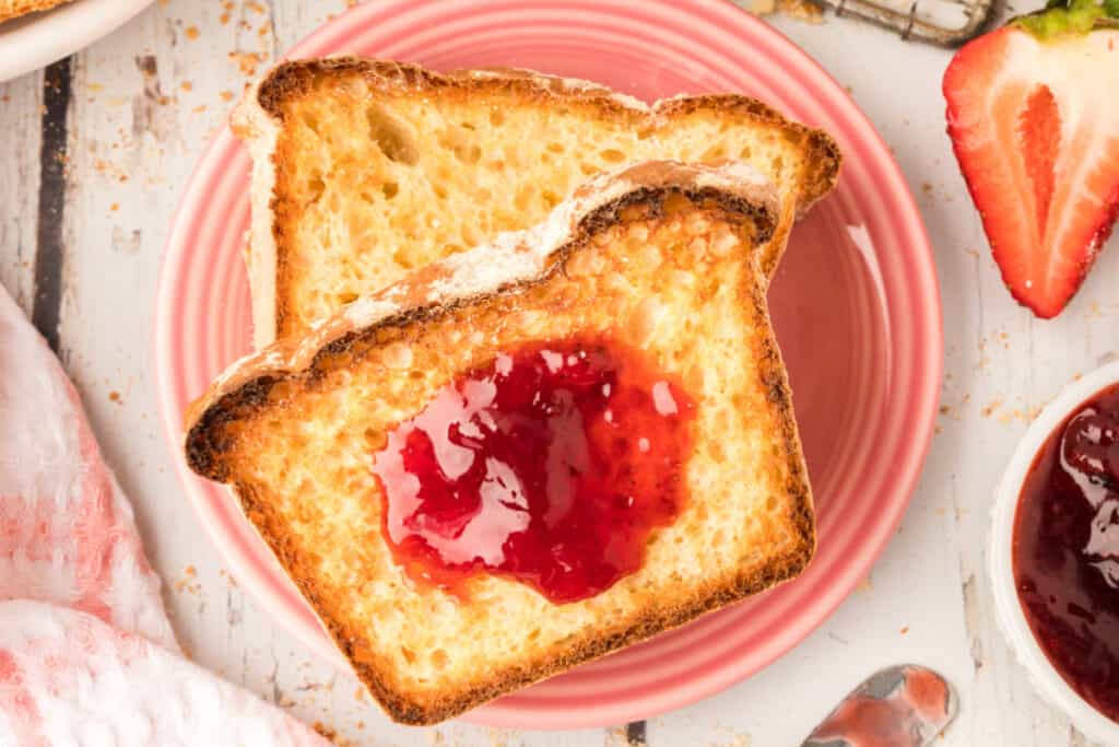 two slices of english muffin bread, one with jam, on plates