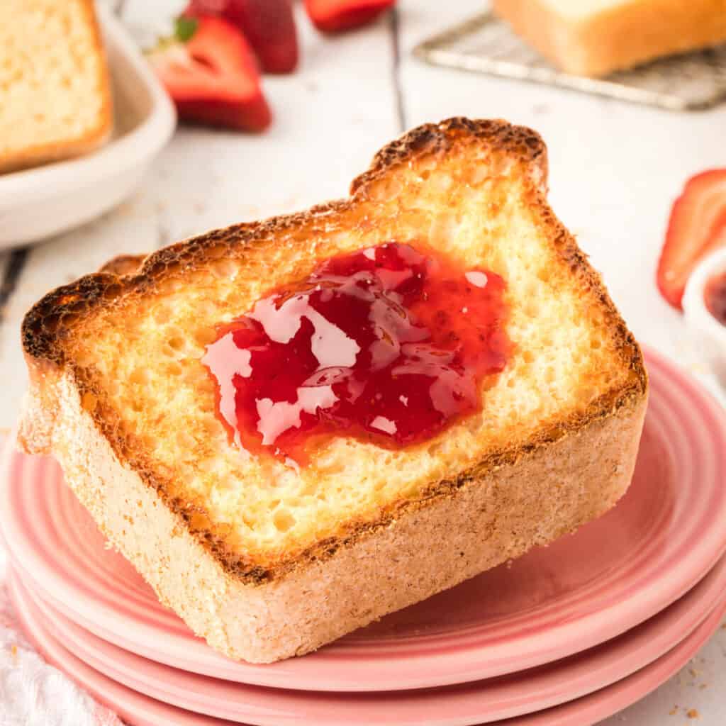 closeup of toasted english muffin bread with jam on pink plates