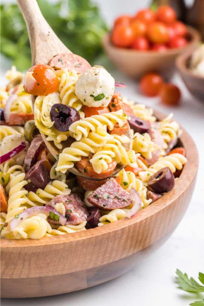 wooden spoon scooping pasta salad from a wooden bowl
