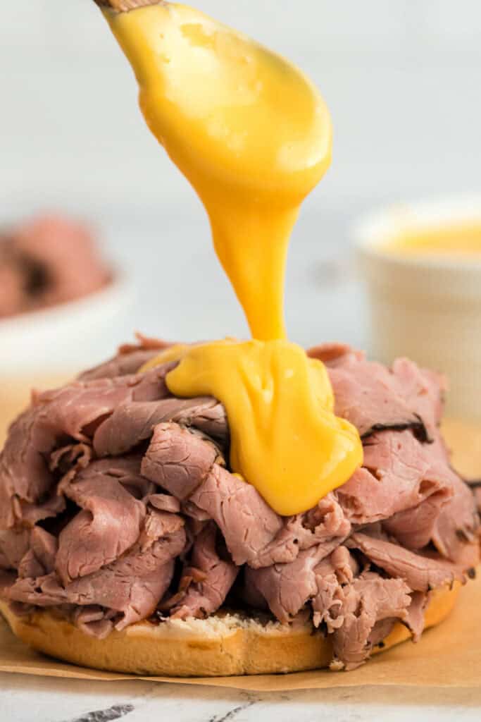 cheese sauce being poured off a spoon onto a sandwich