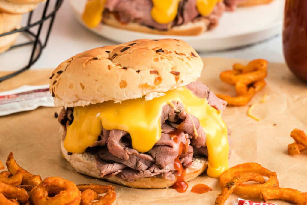 single beef and cheddar sandwich on brown paper with curly fries around