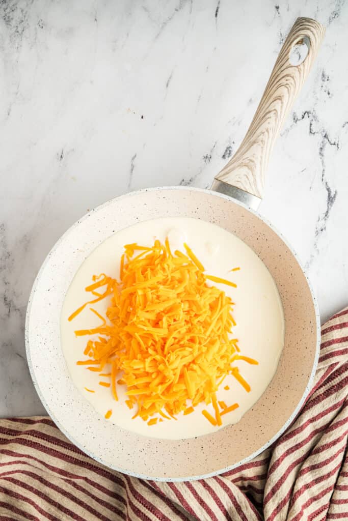 In a non-stick skillet, add the heavy cream and shredded cheddar.